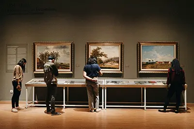 People reading placards in a museum, paintings hang on the walls